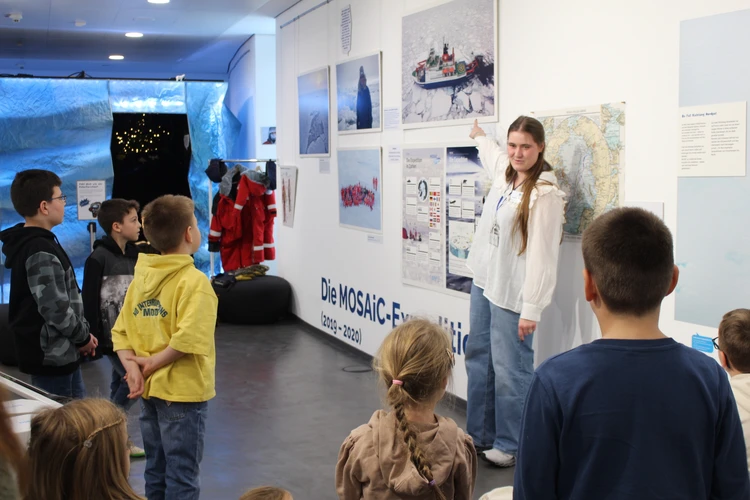 Eine Gruppe von Kindern h&ouml;rt einer Mitarbeiterin in der Artkis-Ausstellung der KLIMA ARENA aufmerksam zu.